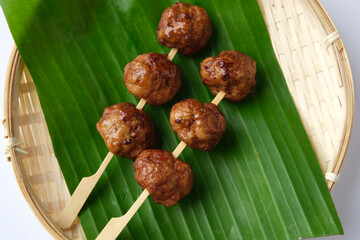 Skewered meatballs served on a banana leaf inside a shallow woven basket.