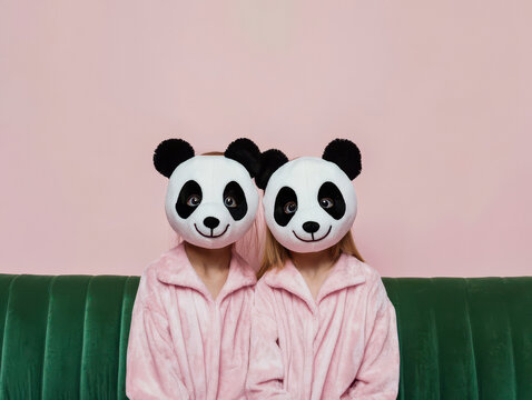 Close-up of two children, one boy and one girl, joyfully wearing panda masks and bamboo pajamas.