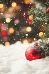 A red ornament sits on top of a snowy ground. The snow is falling around the ornament, creating a peaceful and serene atmosphere