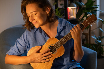 A young girl playing an ukulele and smiling at home, cosy evening and light
