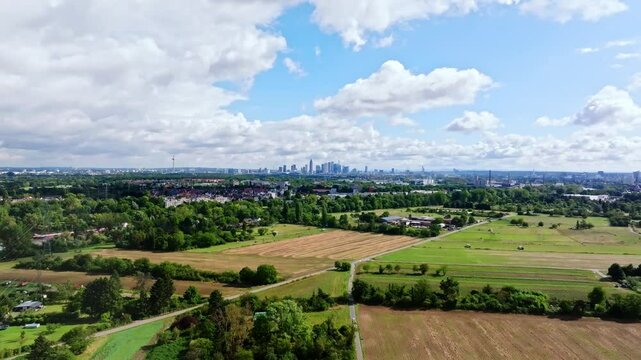 Drone video of Frankfurt's skyline on a partly cloudy day, featuring the Main River in the foreground and adjacent fields. Drone move forward