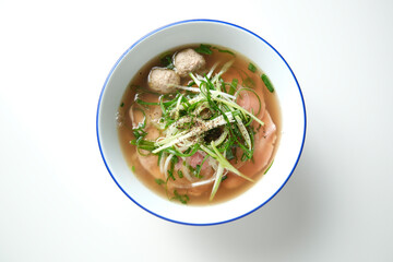 A meatball noodle soup topped with green onions surrounded by spices on the surface.