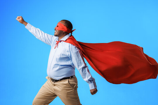 African American overweight guy in superman costume, in flying pose on blue background