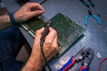 Close-up of hands working on a circuit board with a soldering iron.