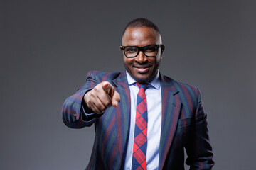 confident african businessman in suit and tie pointing finger at viewer on clear grey background