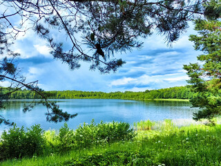 Serene landscape featuring a tranquil lake surrounded by lush greenery and distant hills under a partly cloudy sky in summer