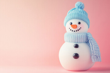 A snowman with a blue hat and a blue scarf is standing on a pink background. The snowman has a happy expression on its face