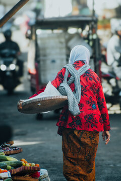 photography of a woman walking wearing red patterned clothes and wearing a jarik which is a Javanese cloth with a batik pattern