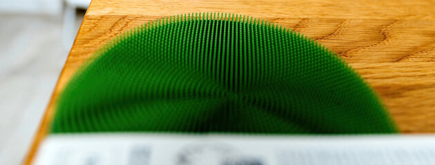 Close-up of a green silicone dish scrubber resting on a wooden surface, showing its texture and...