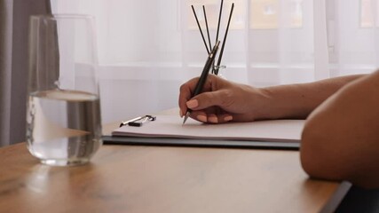 Woman drinking water from glass while writing in notebook. Water helps maintain focus and hydration during work. Ideal for themes of productivity, wellness, and staying refreshed with water.