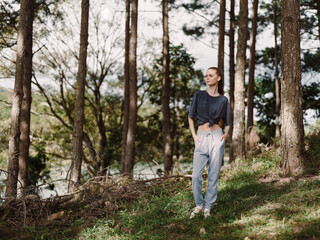 Stylish woman standing in a forest, wearing casual sportswear, enjoying nature with a serene...