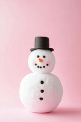 A snowman with a hat and a carrot nose is standing on a pink background. The snowman's expression is happy and playful, and the hat adds a touch of whimsy to the scene