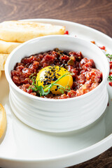 A close-up of a gourmet dish featuring a raw egg yolk on top of finely diced meat, likely tartare, with toast slices on the side. The elegant presentation suggests a fine dining experience.
