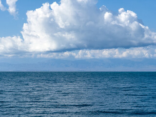 Fototapeta premium Issyk-Kul Lake with a cloudy sky and mountains in the background. The water is calm, reflecting the sky. The serenity and peacefulness of nature in the early morning hours.