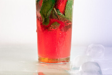Pink drink on a glass table close-up. Pieces of ice and mint in a glass. Juice or cocktail for a party or celebration.