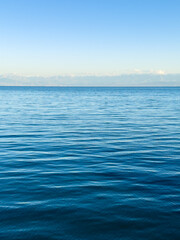 Obraz premium Issyk-Kul Lake with a cloudy sky and mountains in the background. The water is calm, reflecting the sky. The serenity and peacefulness of nature in the early morning hours.