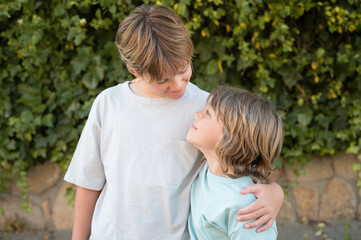 Fototapeta premium Horizontal photograph of two handsome blond caucasian boys hugging and looking at each other with love and positive attitude. Concept of happiness, childhood, brotherhood and healthy friendship.