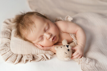 Peaceful newborn sleeping with knitted teddy on soft beige blanket