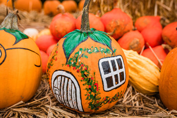 Painted pumpkin and gourds with faces, displayed on straw as Halloween decorations.