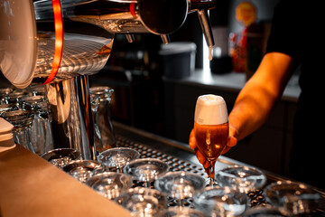 Naklejka premium A bartender skillfully pours a foamy beer into a glass at a modern, stylish bar. The setting features a warm ambiance, highlighting the art of beer serving and hospitality.