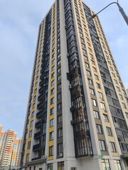 Fototapeta premium A towering residential building with pastel accents, featuring a wide array of windows and balconies. The design reflects the contemporary urban approach to high-density living in city environments.