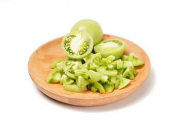 Whole and sliced green tomatoes (Solanum lycopersicum) on a wooden plate against a white background. The photo captures the fresh, juicy, and crisp texture of the slices.