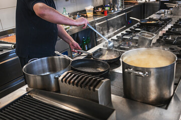 Chef stirring melted cheese in a large pan on a stovetop.