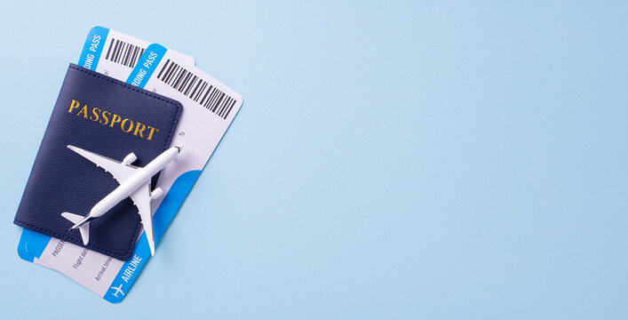 Flat lay image of a passport with airplane model and boarding passes on a light blue background, symbolizing travel and vacation planning