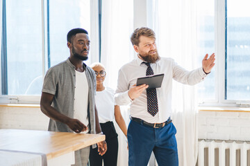 Professional real estate agent showing house to African American attentive couple