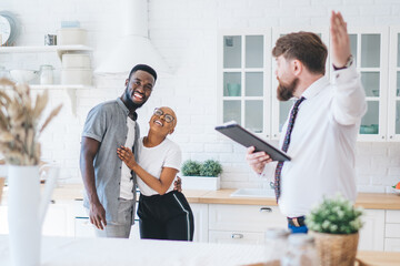 Confident estate agent showing kitchen to African American elated couple