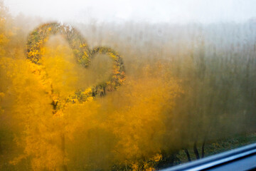 A heart is drawn on a foggy window with trees in the background