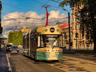 Obraz premium A vintage-inspired tram travels down a quiet street in Saint Petersburg, illuminated by the warm afternoon sunlight. The tram retro design harmonizes with the historic architecture of the city