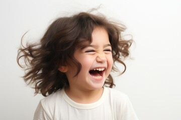 Young girl with curly hair is smiling and laughing. She is wearing a white shirt and she is happy