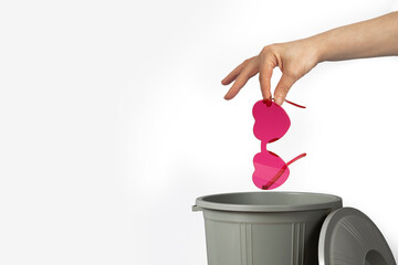 Hand throwing rose-colored glasses into trash bin or waste bucket. Heart-shaped glasses, rejected...