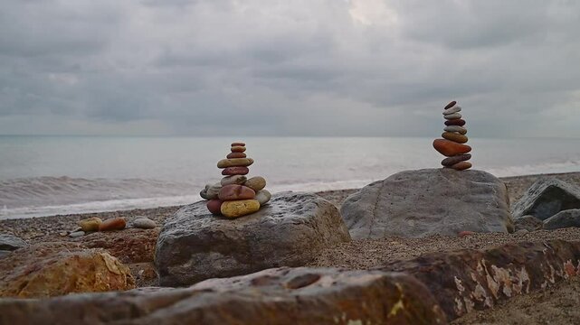 A duo of apachetas, stone mounds beside the sea, under the glow of a reddish autumn afternoon in Spain.