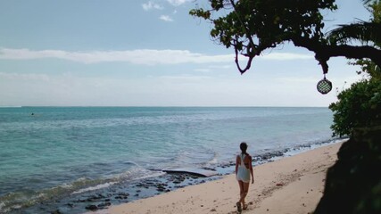 Young woman is walking on a secluded beach, enjoying the peace and quiet of her summer vacation. The turquoise water and white sand create a picturesque setting for a relaxing getaway