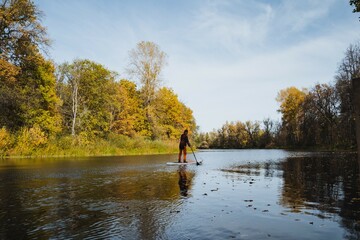 A man is confidently standing on a paddle board, perfectly balanced in the serene middle of a...