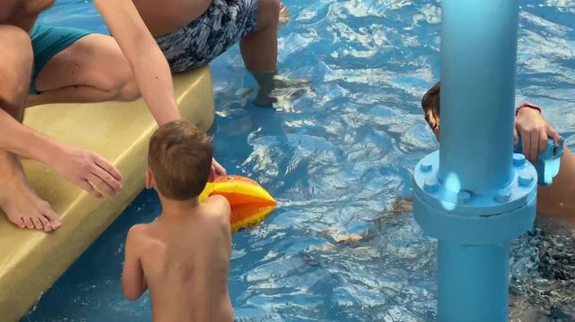 Vilnius, Lithaunia - October 23, 2024 - Two young boys in a pool, one wearing floaties, playing near an adult. Fun and family-friendly water activity in a shallow pool.