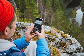 A man, comfortably relaxed on a large rock amidst the wilderness, captures and preserves the...