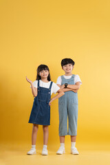 Fototapeta premium Full body image of a kid girl and kid boy posing on a yellow background