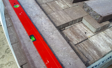 Fototapeta premium Close-up of paving stones being leveled with a red spirit level tool, showcasing construction and landscaping work. Perfect for DIY and home improvement projects.