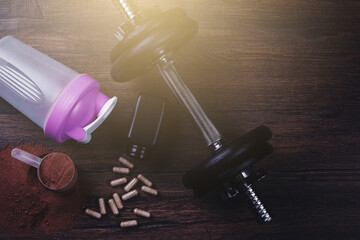 Fitness Supplements, Dumbbell, and Protein Shaker on Wooden Surface