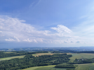 A stunning panoramic view of lush green fields and rolling hills under a bright blue sky with fluffy clouds. Perfect for landscape lovers and nature enthusiasts.