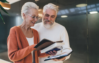Senior man and woman reviewing documents together, smiling and engaged in discussion. Both dressed...