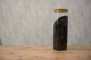 A clear glass container filled with black tea mixture sitting on a wooden table against a light textured background