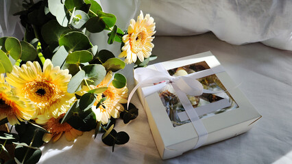 Chocolate covered strawberries in gift box and flowers (yellow gerbera and eucalyptus) on white bed, Valentine's Day dessert, romance, food as a gift.