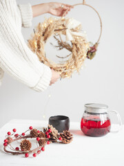 Woman holding a festive wreath with holiday decorations and red herbal tea on a table