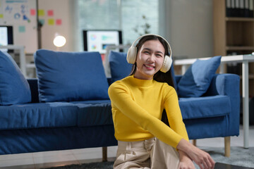 Obraz premium Asian woman wearing headphones and smiling while working remotely in modern office