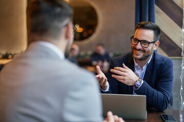 Two mid adult Caucasian businessmen engage in a productive meeting, working on a laptop in the...