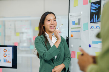 Businesswoman presenting company performance using data analysis charts on whiteboard in office...